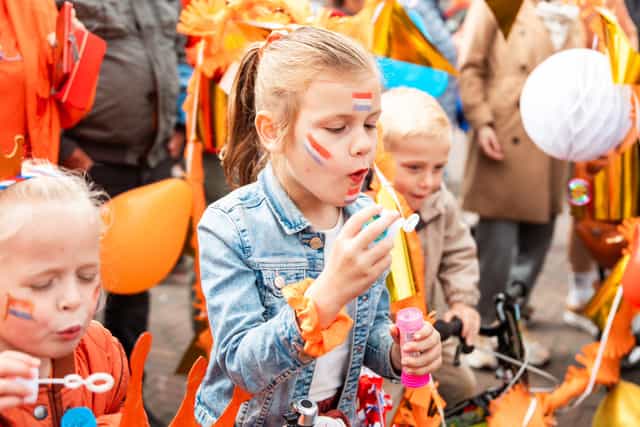 Meisje met rood wit blauwe schmink blaast op een toeter tijdens een oranje feest.