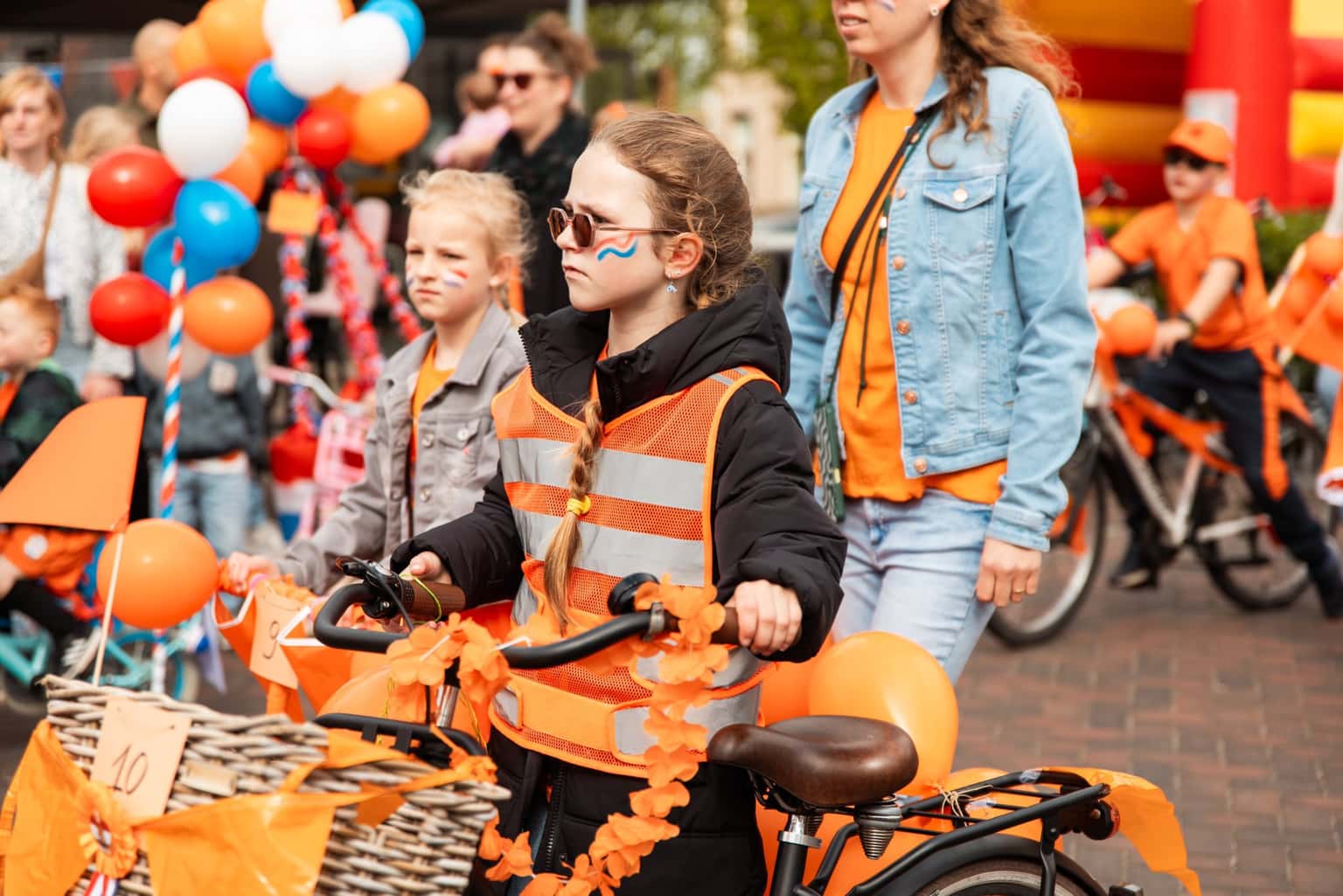 Kinderen fietsen mee in een optocht met versierde fietsen tijdens een oranjefeest in het dorp.